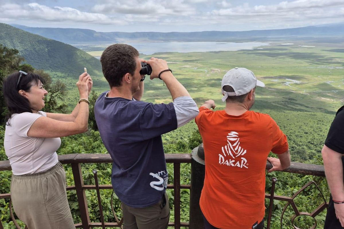Trois voyageurs aux jumelles depuis un point de vue aménagé, accompagnés par un guide en Tanzanie