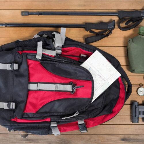 Sac à dos de randonnée, gourde, jumelles et boussole disposés à plat sur un plancher en bois