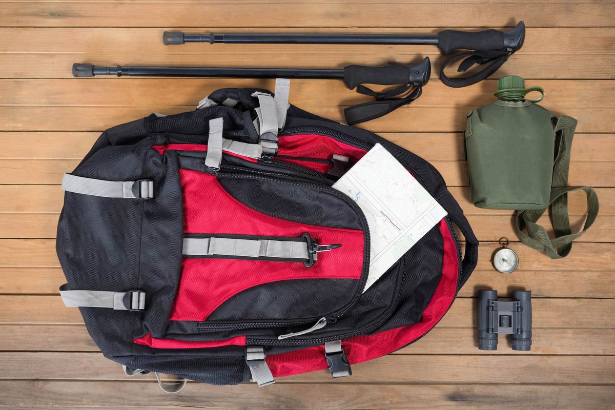 Sac à dos de randonnée, gourde, jumelles et boussole disposés à plat sur un plancher en bois